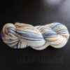 A skein of yarn twisted into a hank, featuring soft, blended shades of cream, beige, light blue, and dark blue, rests on a dark surface. The words "LEILANI HANDMADE" are faintly visible beneath the yarn.