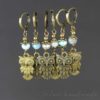 A set of six handmade clip on owl stitch markers featuring brass owl charms. Each pair includes different colored beads: turquoise, grey, and pale blue, above the owl charm. The background is plain and the text "leilani handmade" appears subtly in the lower right corner.