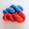 Two skeins of Corriedale handspun hand-dyed yarn are displayed on a white surface. The top skein is a gradient of blue hues, while the bottom skein features shades of red and orange. The text "LEILANI HANDMADE" is faintly visible beneath the skeins.