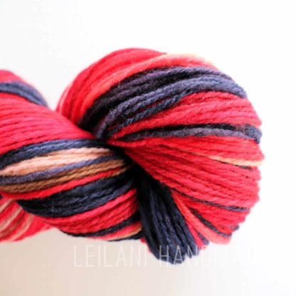 A close-up of a skein of yarn wound into a spiral. The yarn features bold stripes of red, dark blue, pink, and light tan. The background is white, making the vibrant colors of the yarn stand out clearly.