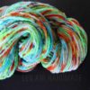 A skein of handspun yarn is coiled on a black surface. The yarn features vibrant colors including green, blue, orange, yellow, and red. Text reading “LEILANI HANDMADE” is faintly visible across the bottom of the image.