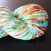 A skein of thick, multicolored yarn with shades of blue, green, orange, yellow, white, and hints of red, displayed against a black background. The yarn has a soft, fluffy texture. The words "LEILANI HANDMADE" appear subtly beneath the skein.