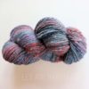 A hank of multicolored, handspun yarn with shades of gray, blue, red, and purple is shown on a white background. The fibers are twisted together, creating a textured, chunky appearance. Faint text at the bottom reads "LEILANI HANDMADE."