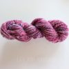 A twisted skein of variegated pink, purple, and blue yarn rests on a white surface. The yarn appears thick and soft, with flecks of white and gold. Light gray text at the bottom reads "LEILANI HANDMADE.