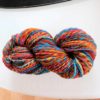A skein of multicolored yarn with vibrant shades of blue, orange, red, yellow, and pink is coiled on a white surface. The yarn is twisted neatly, showcasing its thick, soft texture. Text on the image reads “LEILANI HANDMADE”.