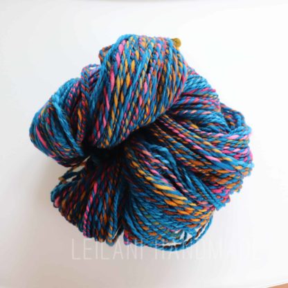 Close-up image of a skein of handspun merino yarn featuring vibrant colors including blue, pink, yellow, and orange. Set against a plain white background.