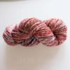 A skein of handspun yarn twisted into a hank, featuring a mix of pink, white, red, and orange tones. The yarn sits on a plain white surface, and the words “LEILANI HANDMADE” appear faintly below it.