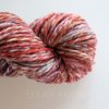 A skein of multicolored yarn twisted into a hank, featuring shades of red, pink, orange, brown, and white, set against a plain white background. The words “LEILANI HANDMADE” are faintly visible near the bottom.