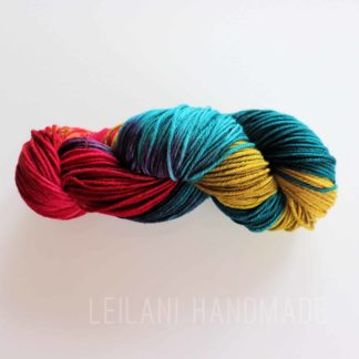 A skein of multicolored worsted weight yarn in shades of red, teal, and yellow, is photographed against a white background. The text "LEILANI HANDMADE" is subtly visible at the bottom of the image.