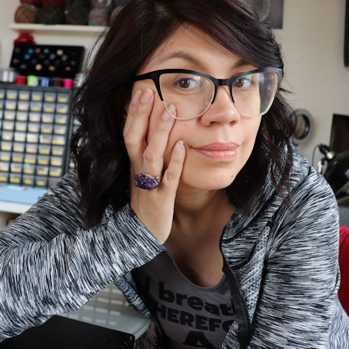 leilani cleveland deveau a woman with dark hair and glasses, sitting at a desk with one hand resting on her face