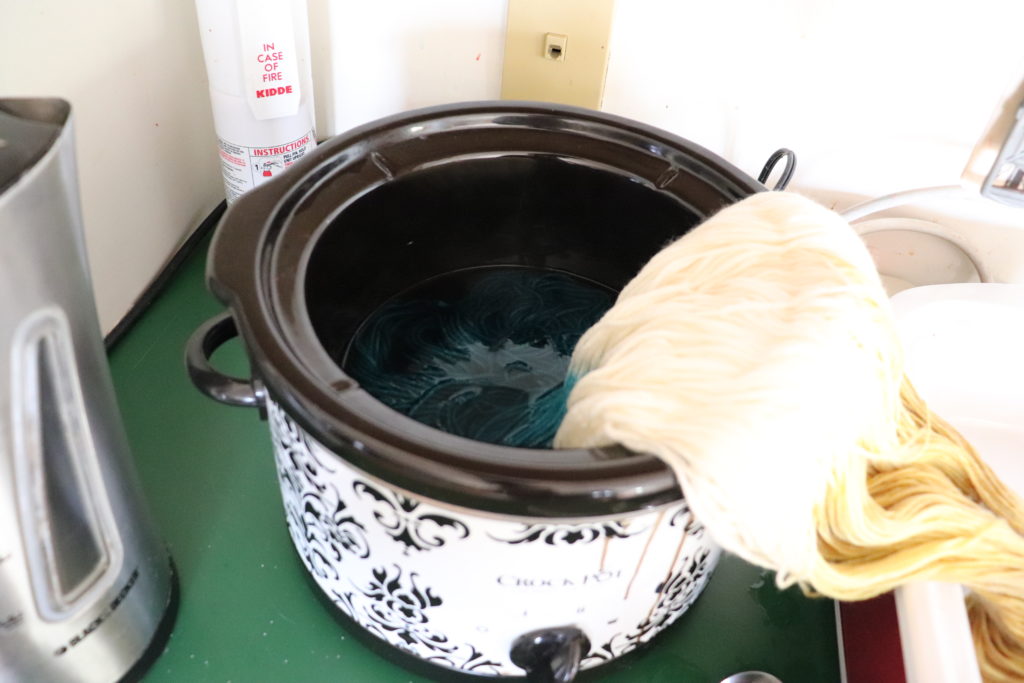 the opposite end of yarn dipped into a crockpot with teal colored dye