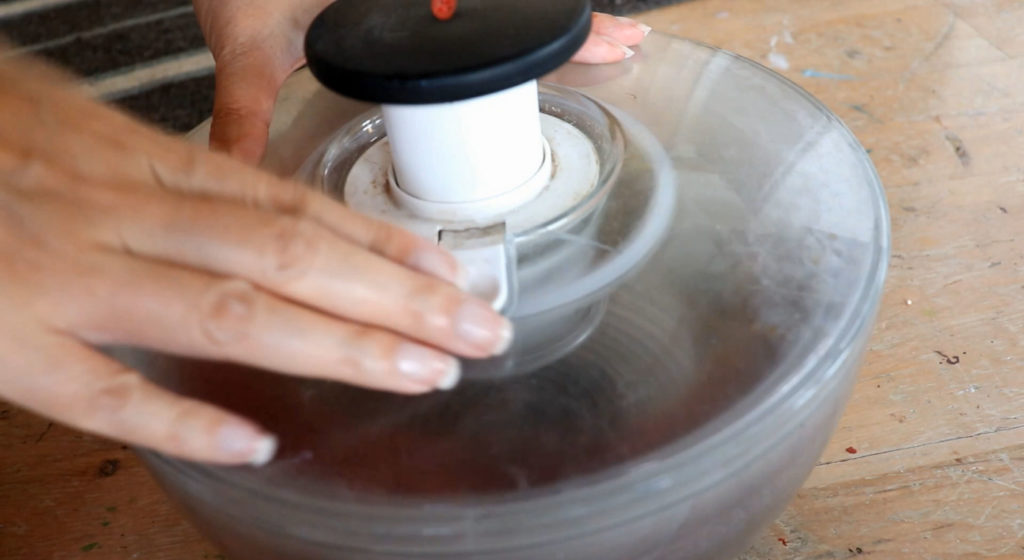 hands rest over a moving salad spinner with yarn inside