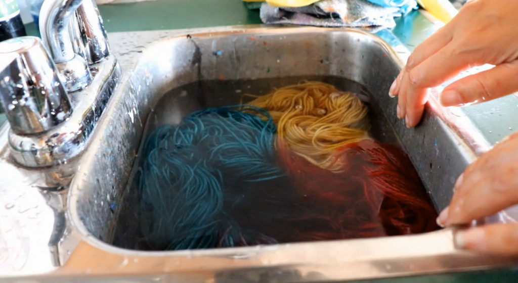 newly dyed yarn in the colors gold, teal and burgundy, rests in a sink filled with water