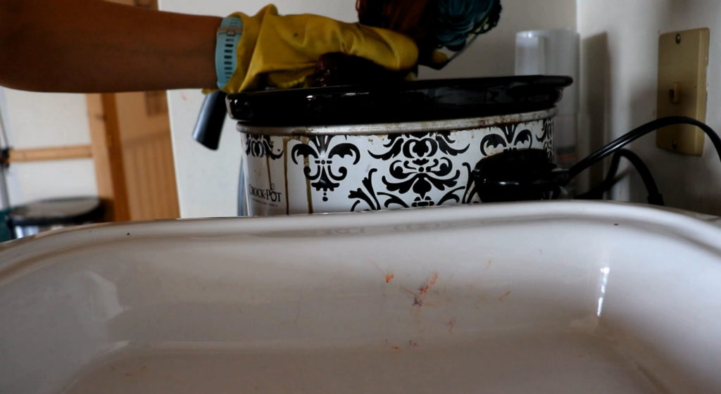 a yellow rubber glove squeezes dye water out of a burgundy section of yarn above a crockpot