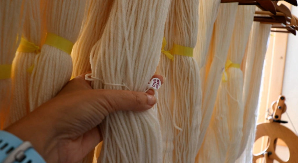 a skein of natural colored yarn with a small round tag with its length and type of yarn