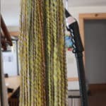 a photo of steam setting spiral ply handspun yarn. In the background you see a garment steamer along side a hung up yellowish-green yarn.