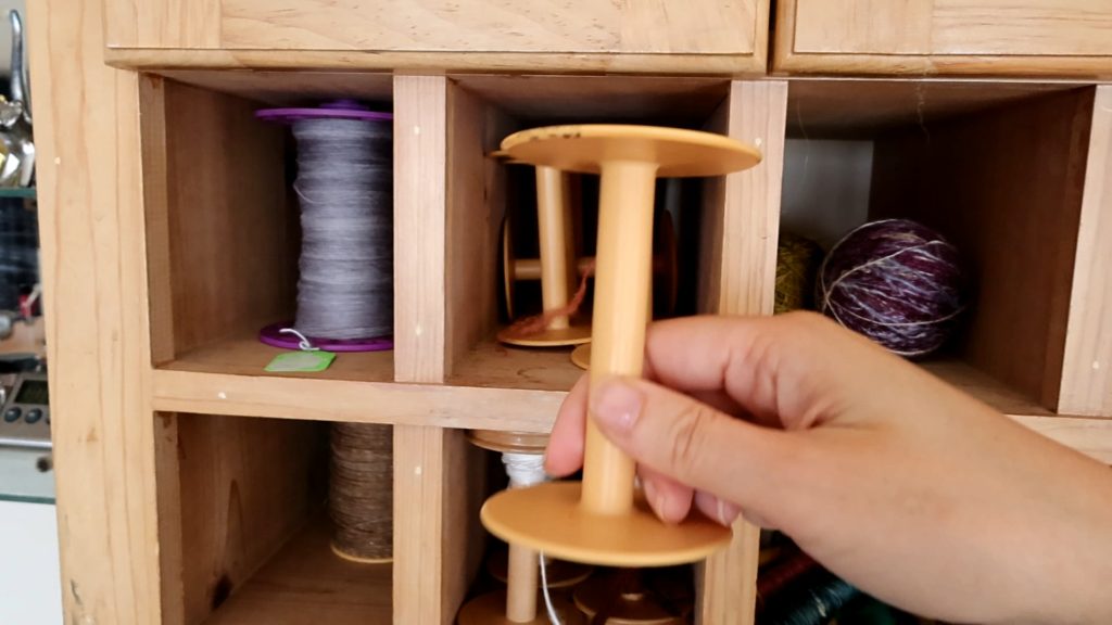 a hand holding a plastic storage bobbin used before plying yarn