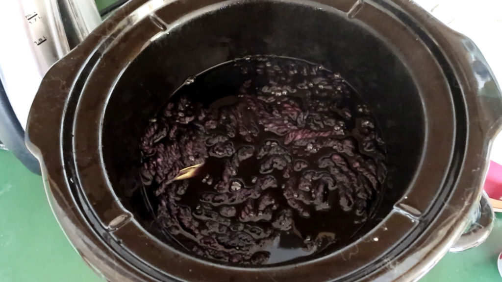 A slow cooker filled with dark grey dye liquor, with a skein of yarn over-dyeing inside a black crockpot 