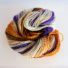 A skein of yarn twisted into a coil, featuring a mix of cream, orange, brown, and purple strands. The colors are blended in a barber pole pattern, and the text “LEILANI HANDMADE” is faintly visible at the bottom of the image. The handspun yarn is entitled, "Lilacs in Autumn".