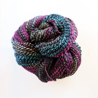 A skein of multicolored handspun yarn called "Bold Vivid Spiral" is coiled on a white background. The yarn features twisted strands of vibrant pink, blue, black, yellow, and white, creating a striking, variegated pattern with a shiny texture.