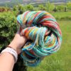 A hand holds a skein of colorful, multicolored yarn in an outdoor setting with green grass, bushes, and a scenic landscape in the background. The words "LEILANI HANDMADE" appear at the bottom.