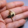 A close-up of a hand holding a delicate gold necklace with a dragonfly pendant and a round initial charm. The pendant has detailed wings, and the charm is engraved with the letter "N." The background is softly blurred.