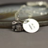 A silver personalized bunny charm necklace with a small, detailed rabbit charm and a round pendant engraved with the letter "B," resting on a smooth stone surface. The background is soft and neutral, emphasizing the jewelry.