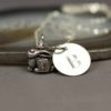 A silver personalized bunny charm necklace with a small, detailed rabbit charm and a round pendant engraved with the letter "B," resting on a smooth stone surface. The background is soft and neutral, emphasizing the jewelry.