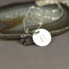 A silver necklace with a small rabbit charm and a round disc engraved with the letter “B,” displayed on a polished agate slice. The background is a soft gray, and “LEILANI HANDMADE” is faintly visible at the bottom.