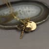 A gold necklace with a dragonfly charm and a round pendant engraved with the letter "N" lies atop a polished agate slice. The background is neutral, and the words "LEILANI HANDMADE" are subtly visible in the lower right corner.