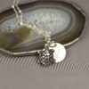 A silver turtle pendant and a round charm engraved with the letter "V" rest on a silver chain, displayed on a sliced agate stone with earthy tones. The background is light gray, and "LEILANI HANDMADE" is subtly visible at the bottom.