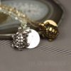 Custom turtle necklace: Two turtle-shaped pendants, one silver and one gold, lie on chains beside a round, engraved disc on a gray stone surface. The background features a sliced agate. The words "LEILANI HANDMADE" are faintly visible in the lower right corner.