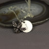 A silver necklace with two pendants: a detailed bee charm and a round disc engraved with the letter "J." The necklace is displayed on a slice of agate and rests on a gray surface. The words "LEILANI HANDMADE" are faintly visible at the bottom.