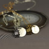 Two necklaces rest on a sliced agate dish: one silver with a round pendant engraved “V” and a silver ladybug charm, and one gold with a round pendant engraved “L” and a gold ladybug charm. “LEILANI HANDMADE” is faintly visible in the background.