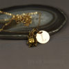 A gold necklace with a ladybug charm and a round pendant engraved with the letter "L" rests on an agate slice. The background is a smooth, dark surface, and the text "LEILANI HANDMADE" is faintly visible at the bottom.