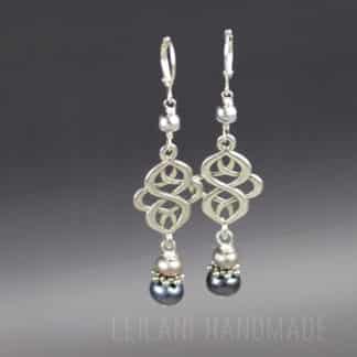 Two dangle earrings with intricate silver loops, each featuring a white and a black pearl bead at the bottom, a small grey pearl with silver bead caps at the top. The earrings hang against a gray gradient background with faint "LEILANI HANDMADE" text at the bottom.